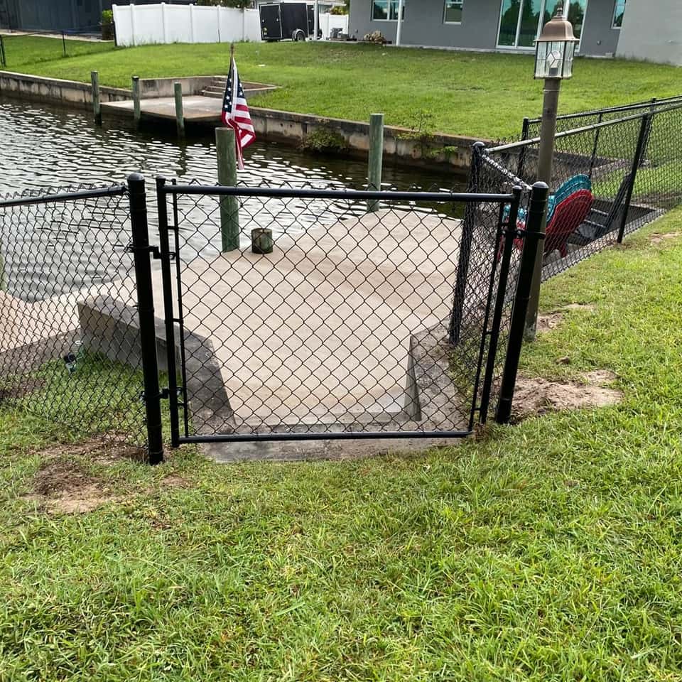 Black chain link fence enclosing a waterfront dock area on a canal-front home — Lobo Fences LLC, Southwest Florida