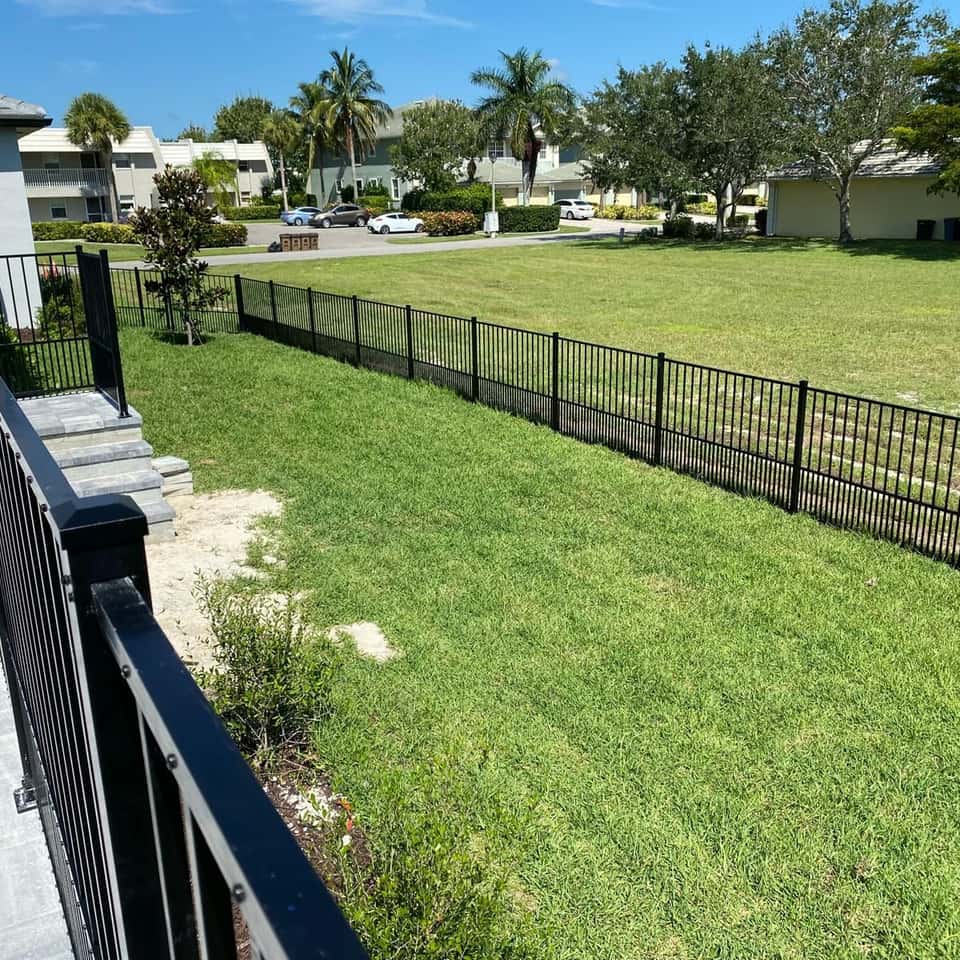 Black aluminum picket fence running along a wide open lawn beside a condo community — Lobo Fences LLC, Southwest Florida