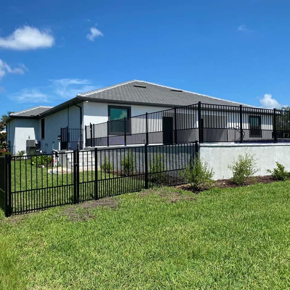 Black aluminum pool fence installed on a low retaining wall at a single-story home — Lobo Fences LLC, Southwest Florida