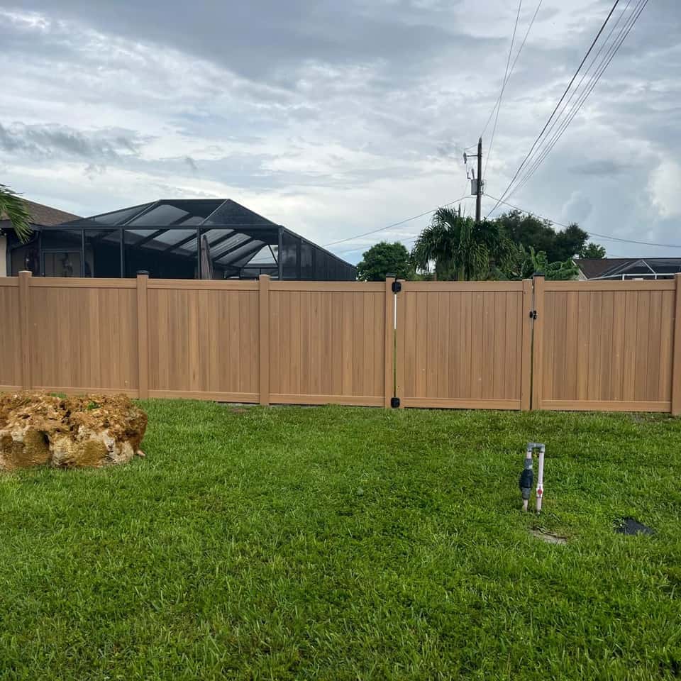 Cedar-tone vinyl privacy fence with a double drive gate in a backyard — Lobo Fences LLC, Southwest Florida
