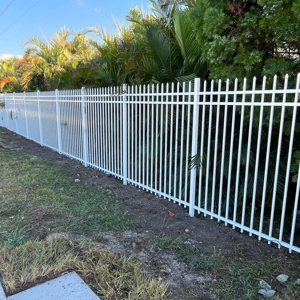 White aluminum spear-top fence along a tropical landscaped property line — Lobo Fences LLC, Southwest Florida
